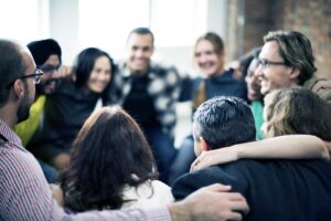 A diverse group of people smile and embrace in a support group, demonstrating the power of a safe therapeutic community to foster connection, understanding, and shared healing.A diverse group of people smile and embrace in a support group, demonstrating the power of a safe therapeutic community to foster connection, understanding, and shared healing.