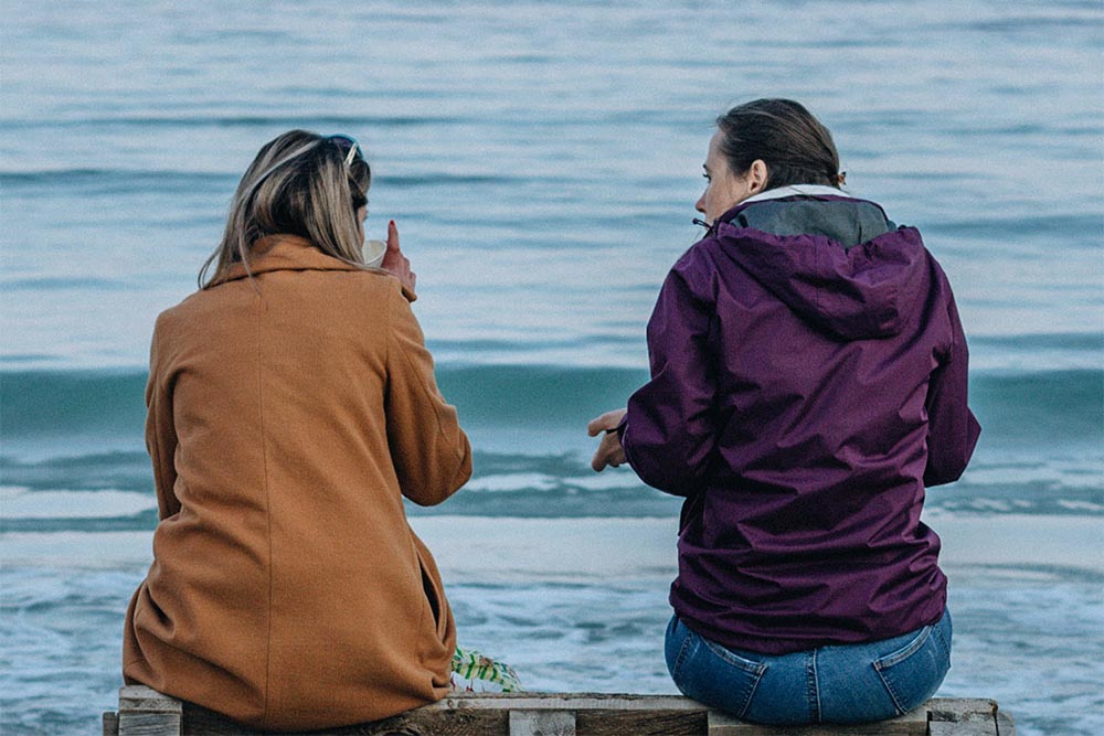 a female sponsor friend listening to her friend sitting in front of the ocean