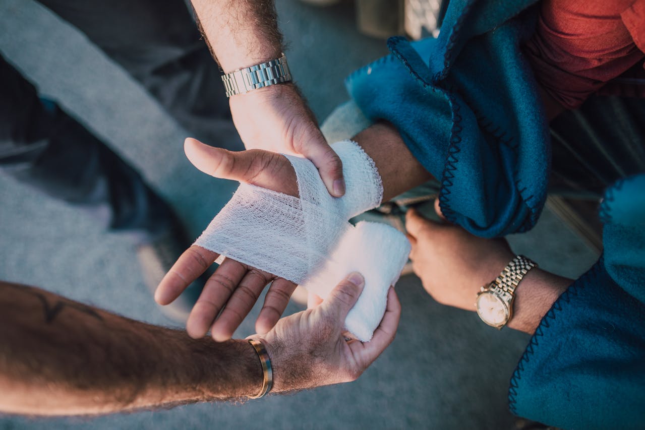 Hands carefully wrap a bandage around a wounded hand, symbolizing the process of healing emotional trauma and psychological wounds with the support of therapy and community.